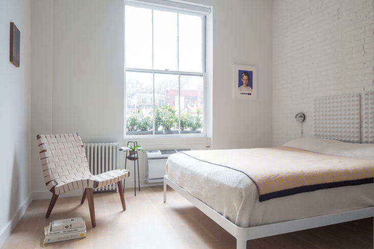 The peaceful bedroom in the back of the apartment is kept simple, with few furnishings, minimal window dressings, and light colors. In lieu of a bookshelf, a few titles are stacked neatly beside a chair.