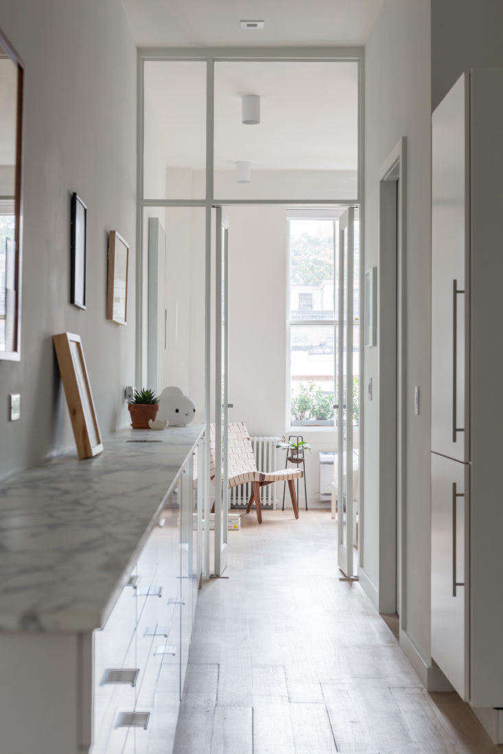 The architects opted to move all of the utilities and appliances for both the bathroom and kitchen to one side of the apartment. It’s a simple concept, but the result is a bright walk-through kitchen, no longer boxed-in and dark, with appliances on the right side and a place to hang art on the left. To add to the open feeling, Dvir and Rauchwerger replaced the solid wall going into the bedroom with a glass partition, which can be covered with a curtain for privacy.
